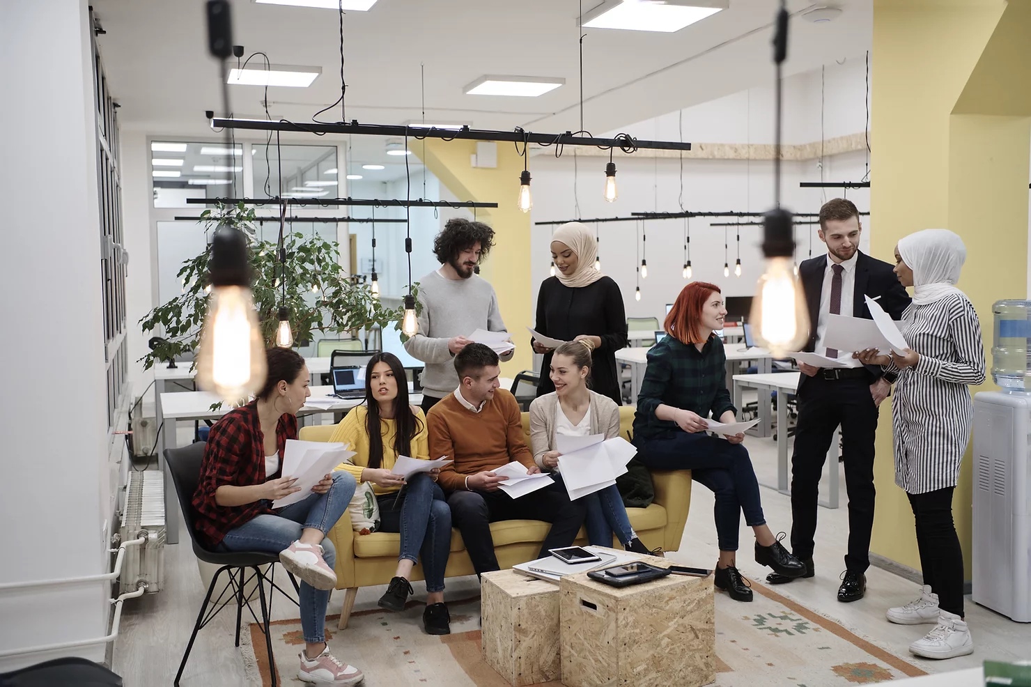 a large group of young diverse business people talking to eachother and holding papers in their hands in large modern office