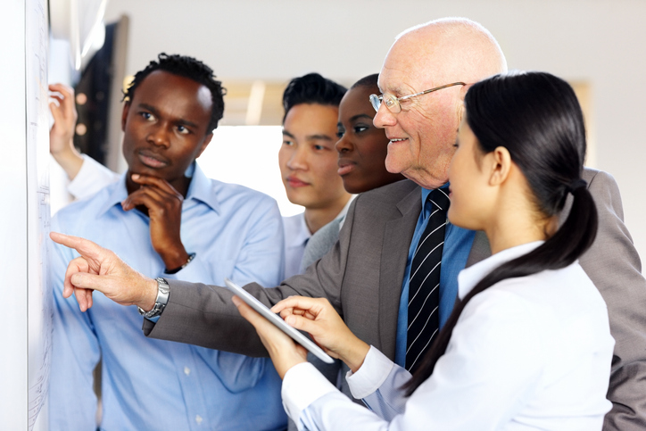 medium shot of mixed race business people discussing new building plan during a meeting at whiteboard